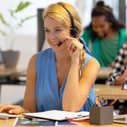 Front view of happy Caucasian female customer service executive talking on headset and working on computer in a modern office